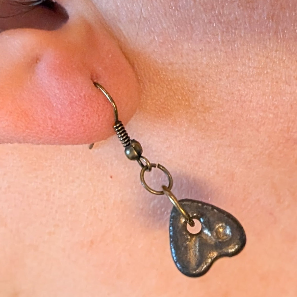 Close-up of a person wearing a heart-shaped earring with a visible clasp.
