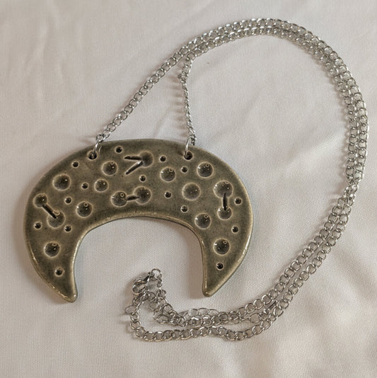 Silver necklace with a unique ceramic crescant pendant on a white fabric background