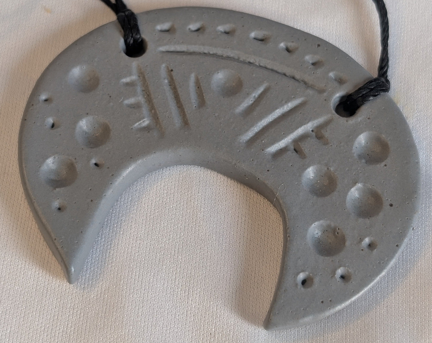 Gray ceramic crescent pendant with engraved design on a black cord