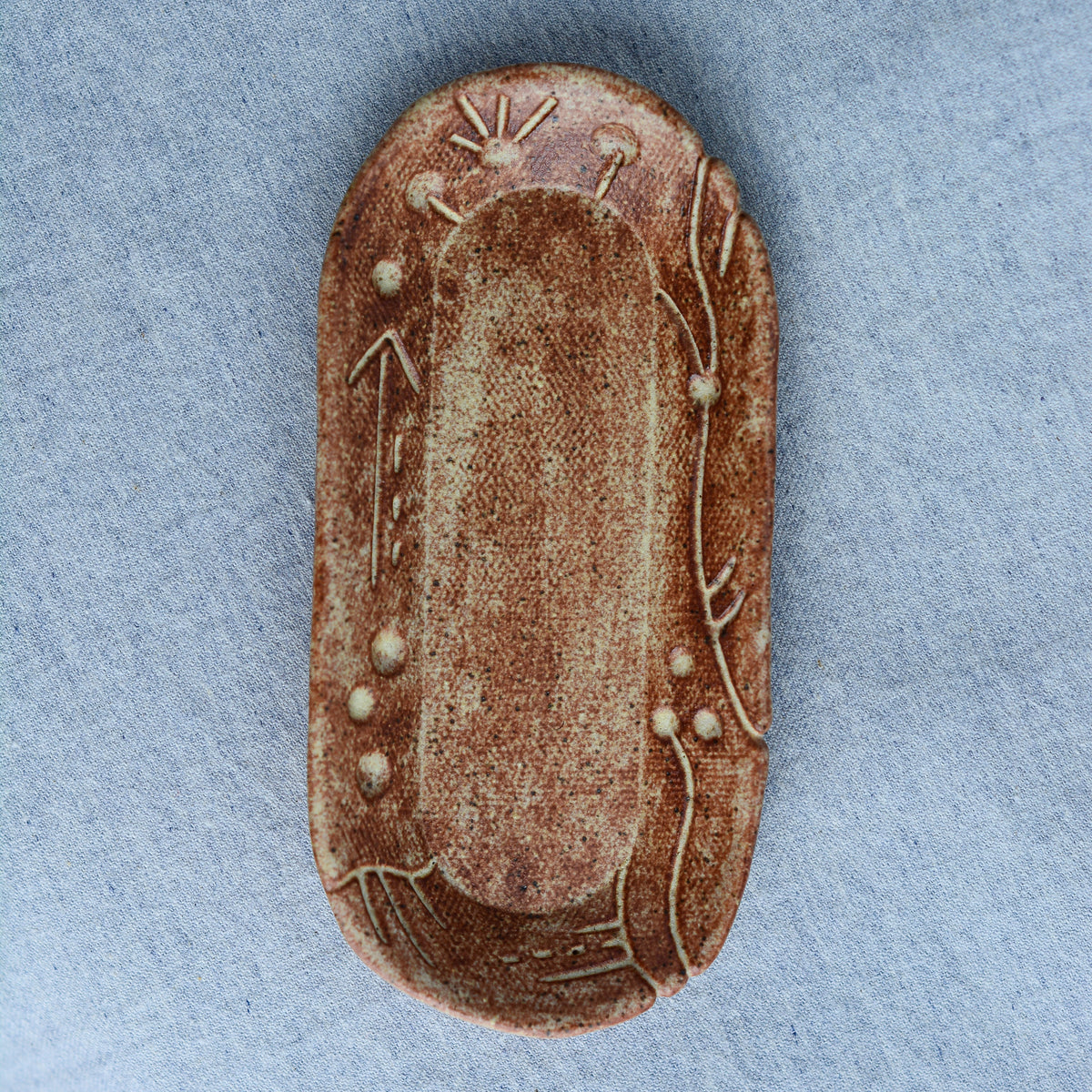A charming oblong dish, ideal for holding rings, keys, or a splash of soy sauce. Each piece is unique, showcasing a distinctive hand-carved motif and a matching hand-painted finish.