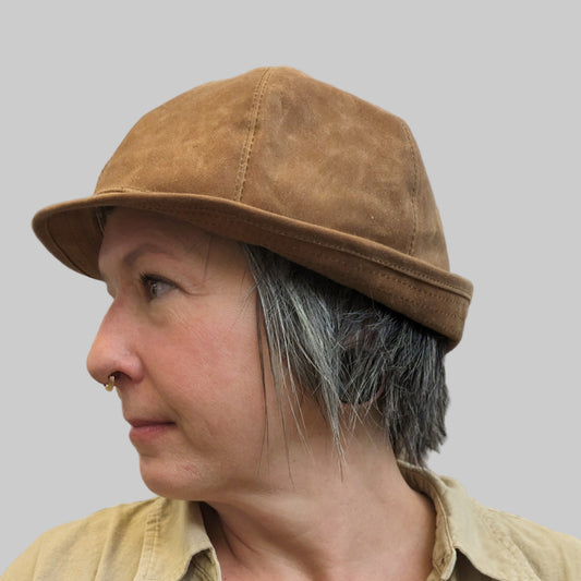 Person wearing a brown hat, beige jacket, and black top with tattoos visible.