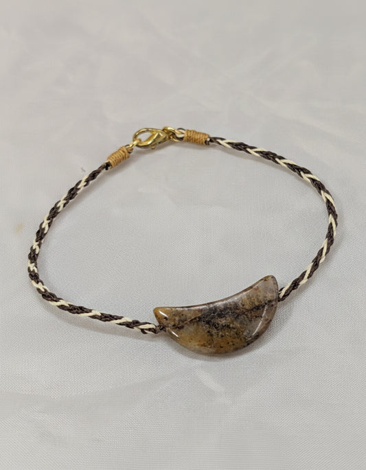 Bracelet with a crescent-shaped stone pendant on a braided cord against a light gray background