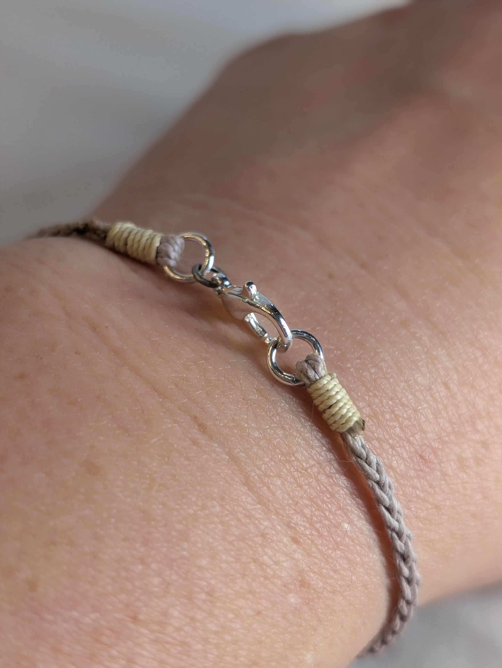 Bracelet with braided design and silver clasp on a wrist against a neutral background