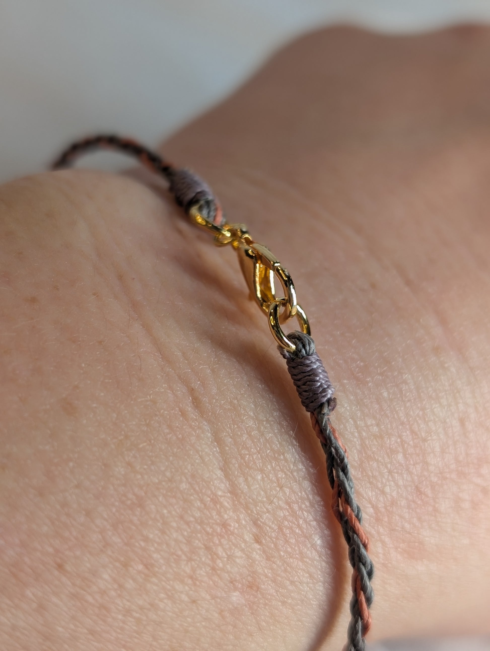 Bracelet with gold clasp on a wrist against a neutral background