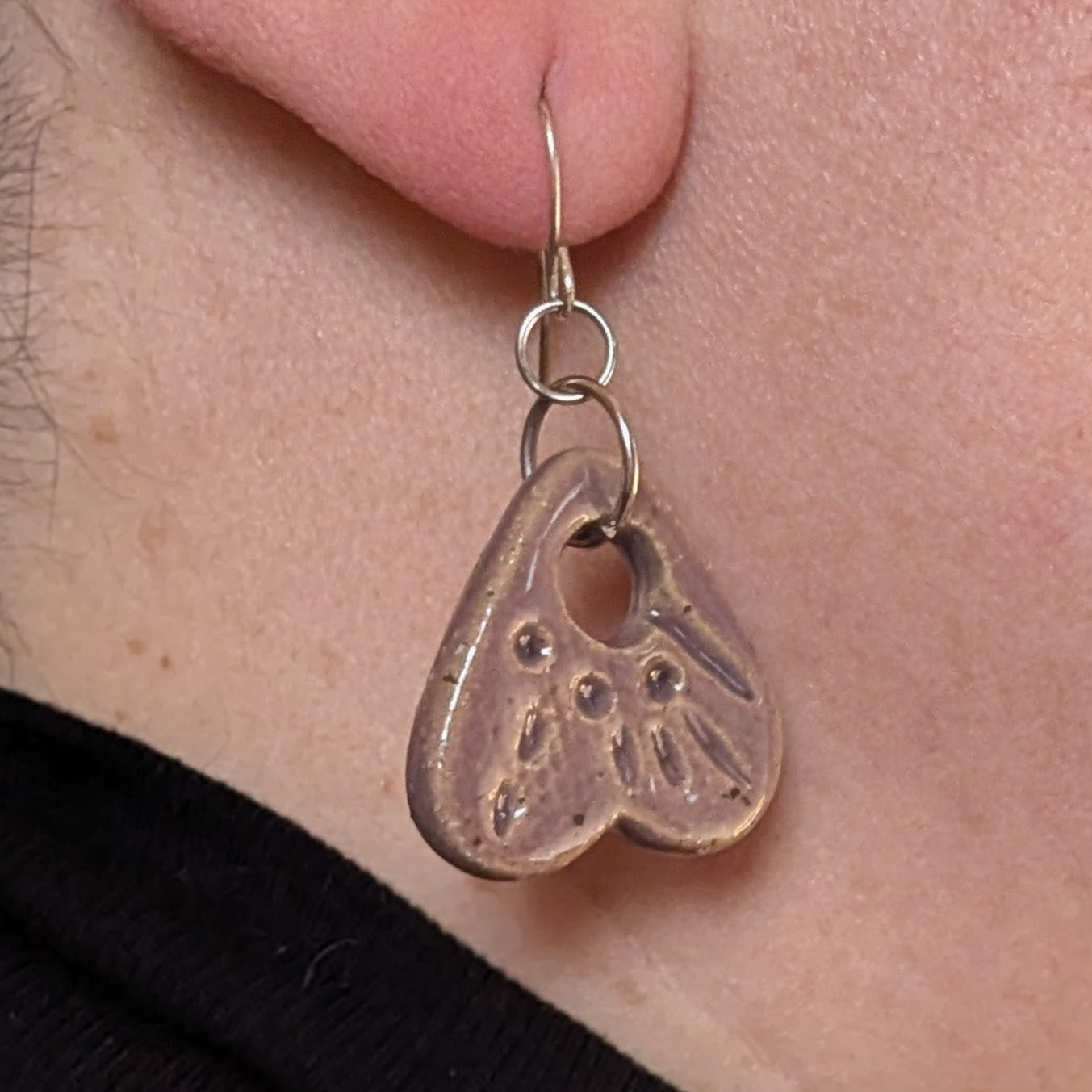 Close-up of a person wearing a silver earring with a heart design.