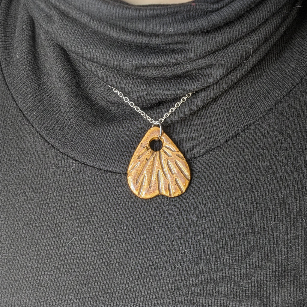 Silver necklace with a rust colored ceramic pendant on a person wearing a dark turtleneck