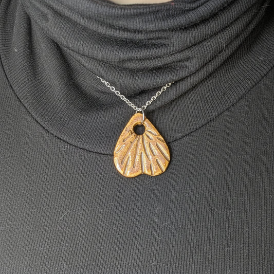 Silver necklace with a rust colored ceramic pendant on a person wearing a dark turtleneck