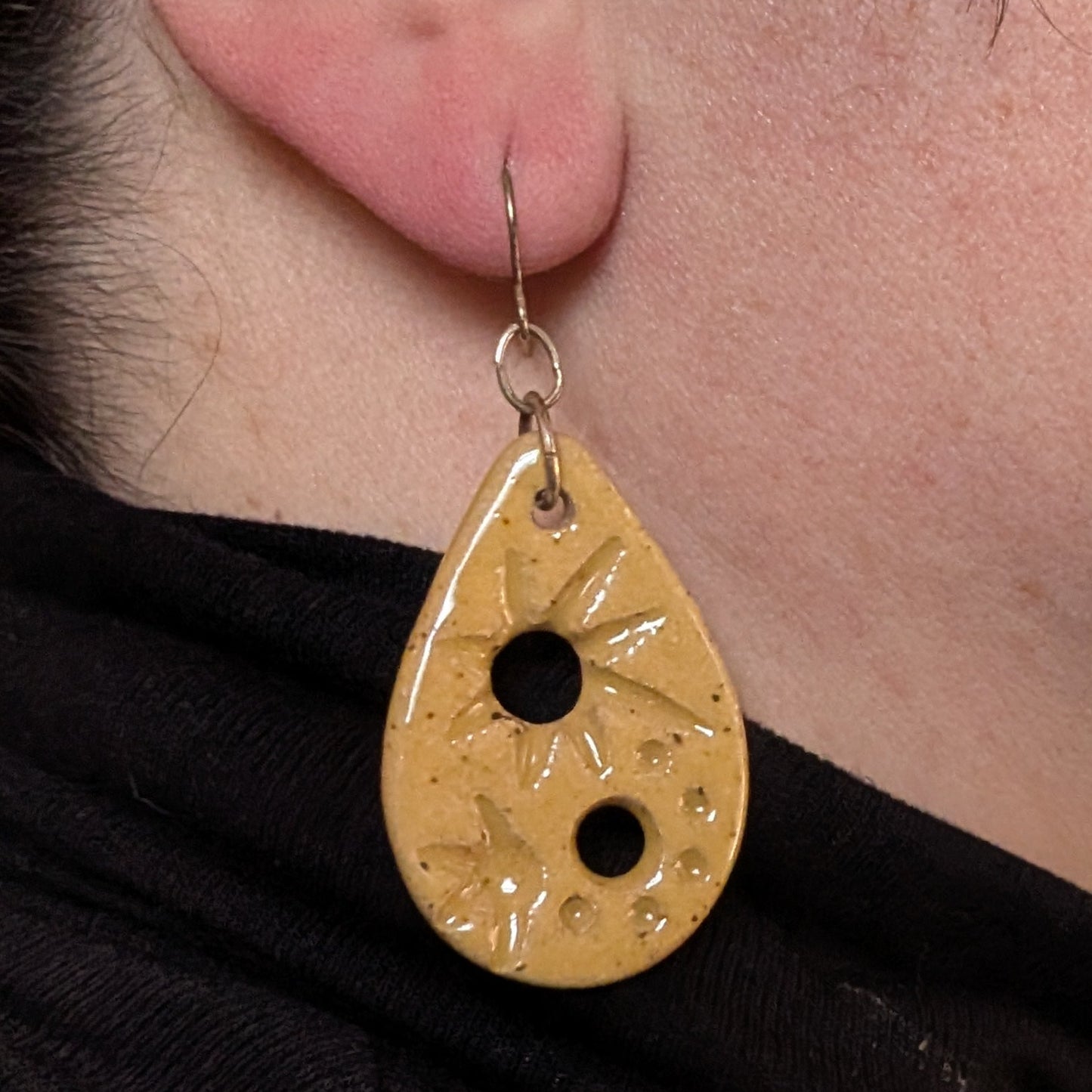 Close-up of a person wearing a gold teardrop earring with a black center.