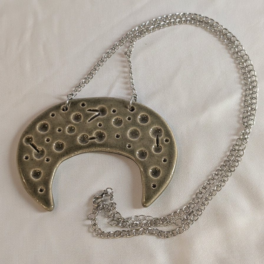 Silver necklace with a unique ceramic crescant pendant on a white fabric background