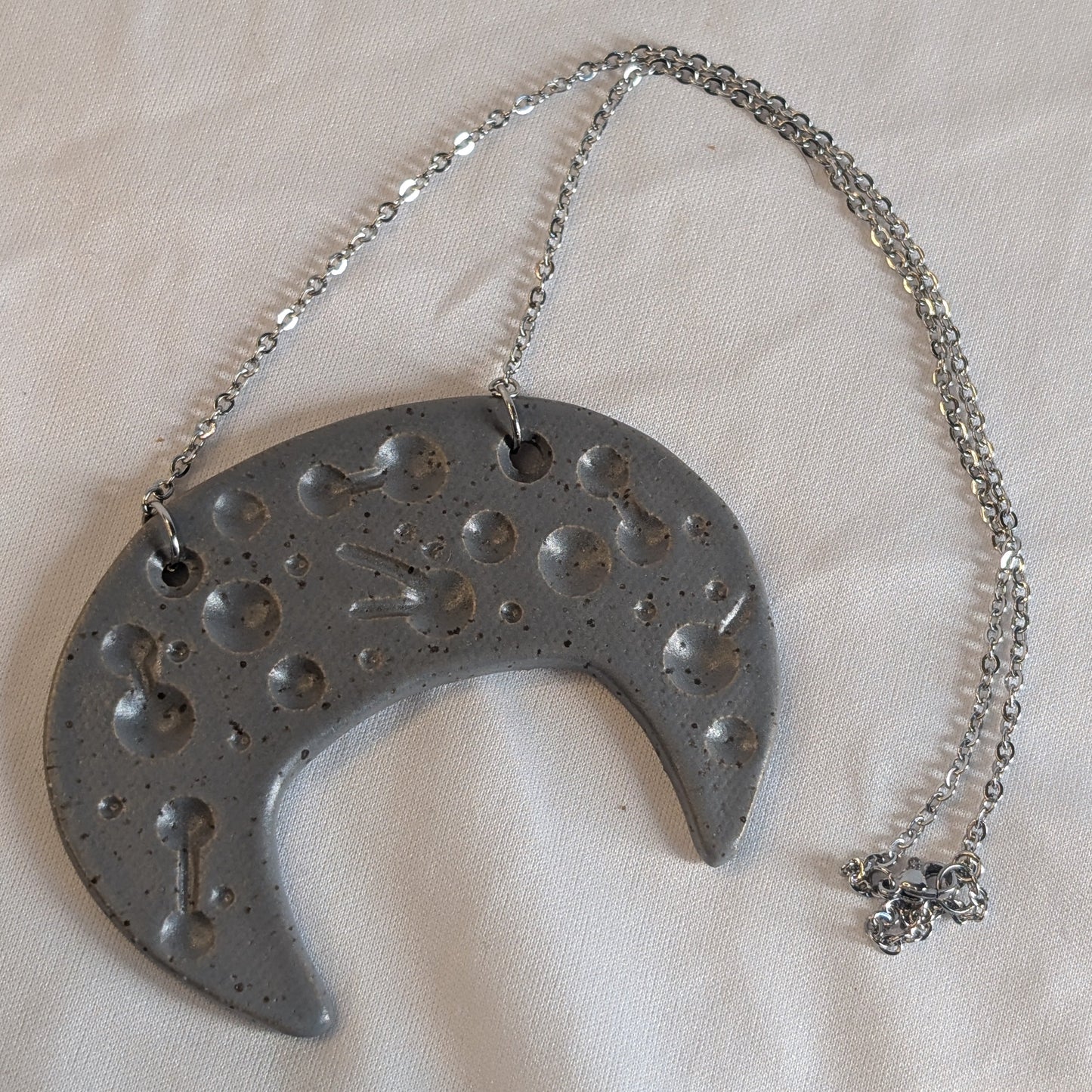 Metallic crescent moon-shaped pendant with chain on a white fabric background