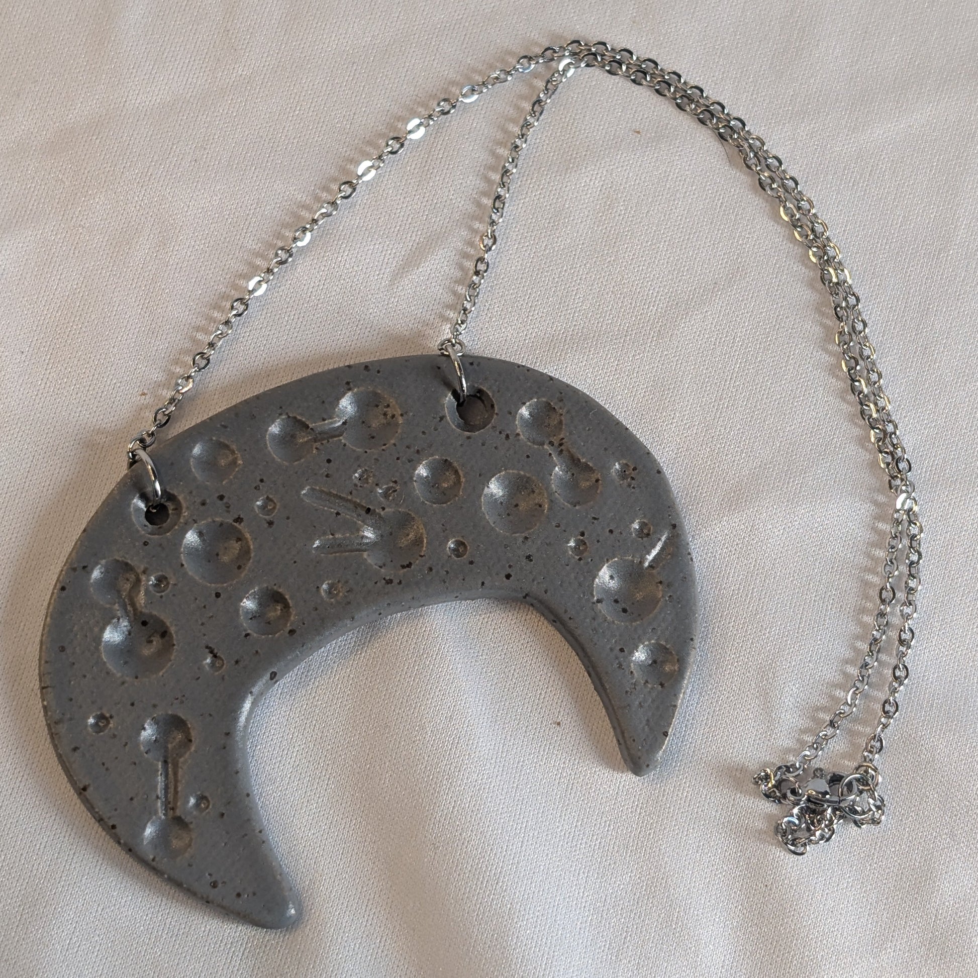 Metallic crescent moon-shaped pendant with chain on a white fabric background