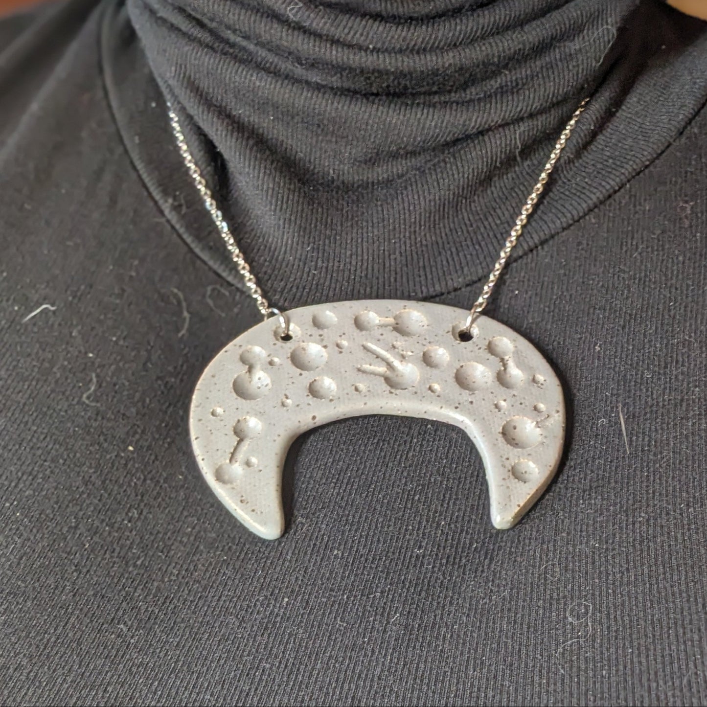 Person wearing a dark gray turtleneck with a unique silver necklace pendant.