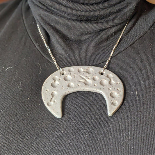 Person wearing a dark gray turtleneck with a unique silver necklace pendant.
