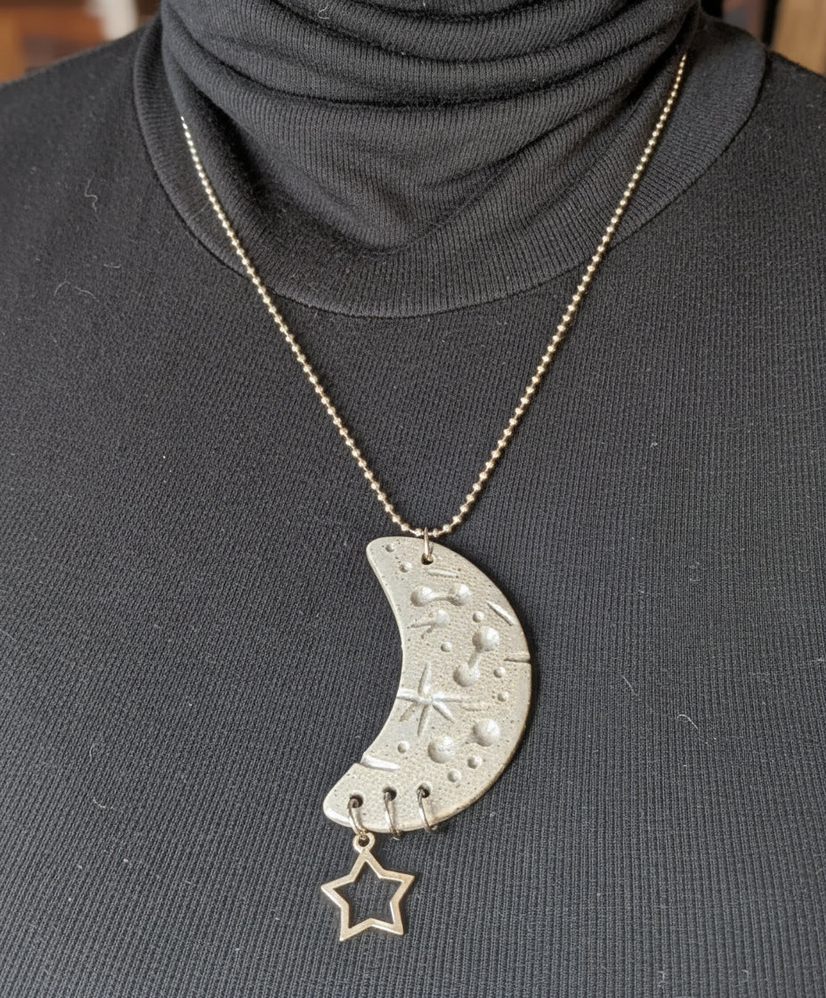 Person wearing a black turtleneck with a ball chain necklace featuring a crescent moon and star pendant.