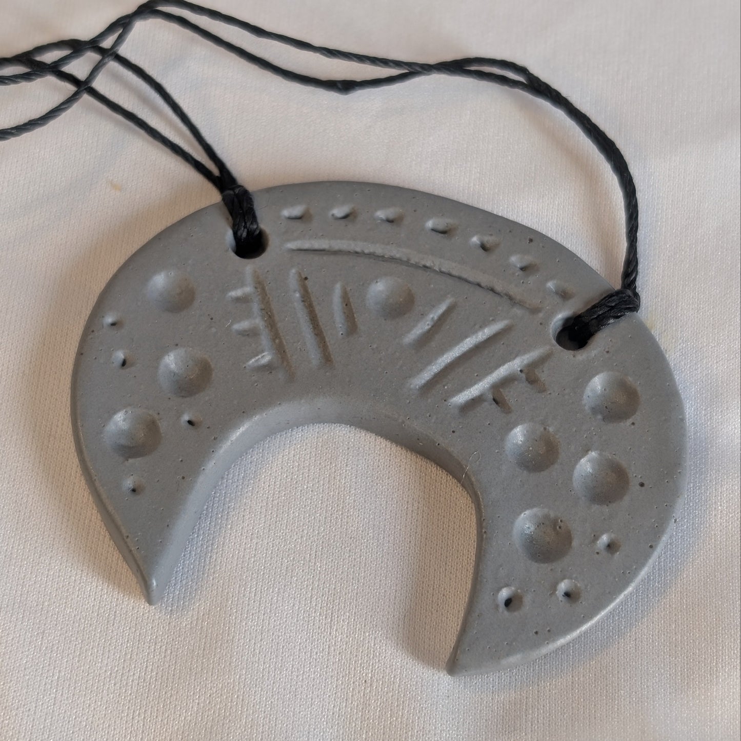 Gray pendant with decorative patterns on a black cord against a beige background