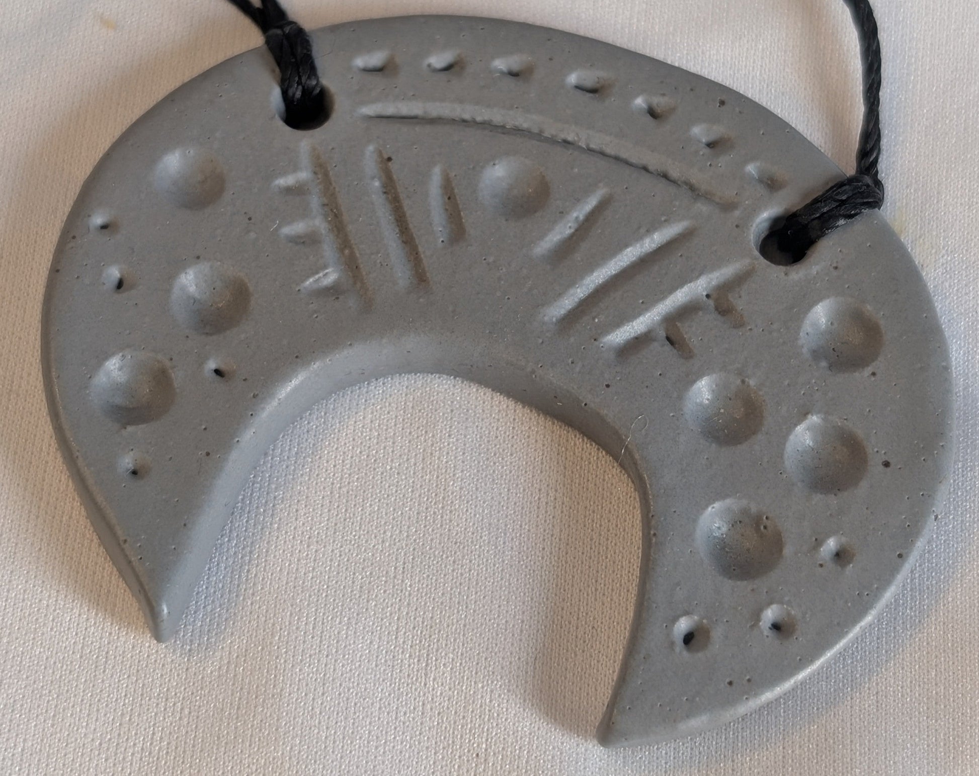 Gray ceramic crescent pendant with engraved design on a black cord