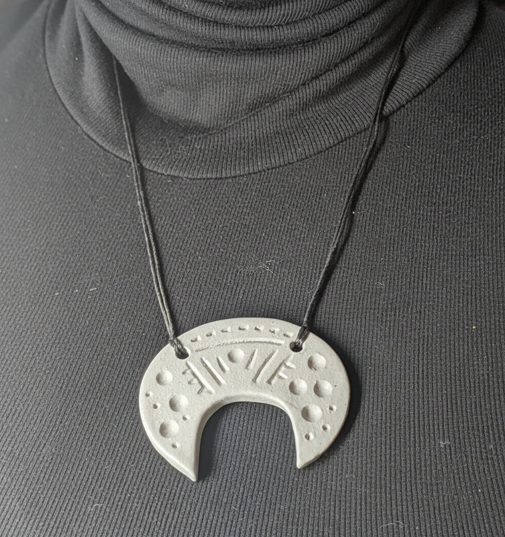 Necklace with a unique pendant worn by a person in a dark sweater.