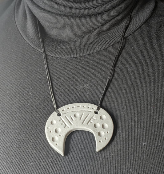 Necklace with a unique pendant worn by a person in a dark sweater.