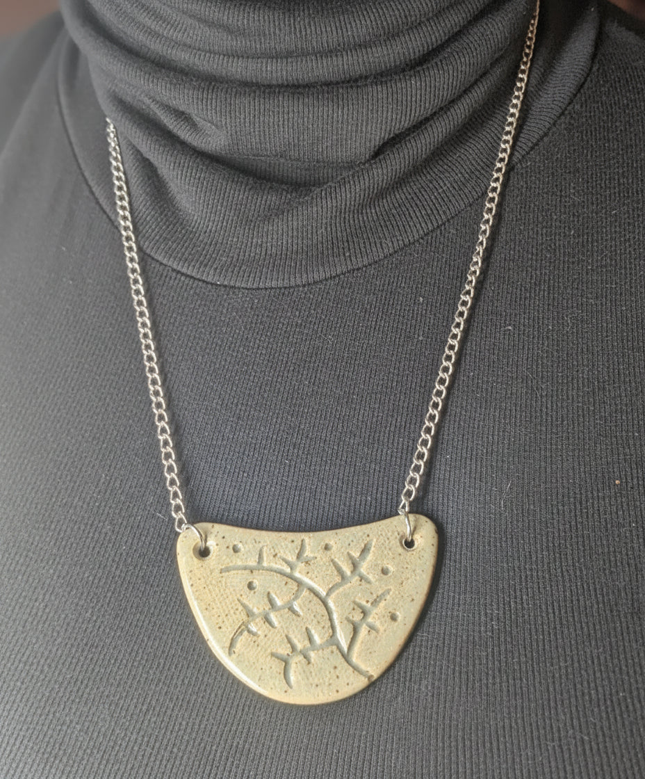 Person wearing a dark turtleneck with a silver necklace featuring an engraved ceramic crescent pendant.