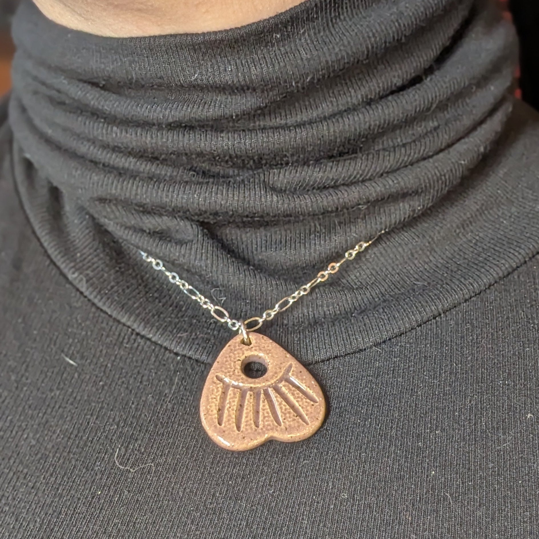 Person wearing a gray turtleneck with a necklace featuring a heart-shaped pendant.