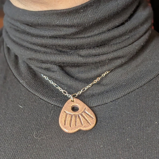 Person wearing a gray turtleneck with a necklace featuring a heart-shaped pendant.