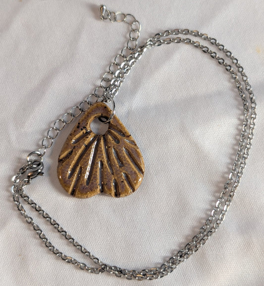 Silver necklace with a carved ceramic pendant on a white fabric background