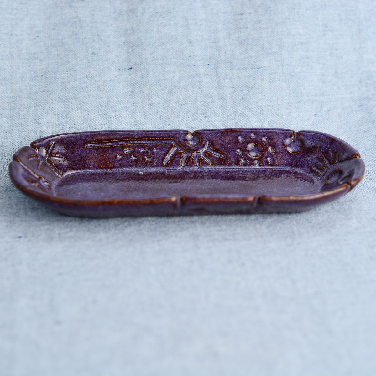 A charming oblong dish, ideal for holding rings, keys, or a splash of soy sauce. Each piece is unique, showcasing a distinctive hand-carved motif and a matching hand-painted finish.