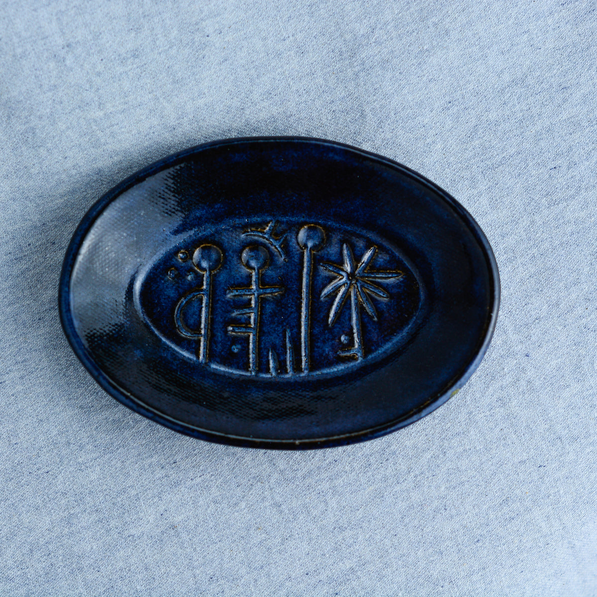 An oval shaped dish, ideal for holding rings, keys, or a splash of soy sauce. Each piece is unique, showcasing a distinctive hand-carved motif and a matching hand-painted finish.