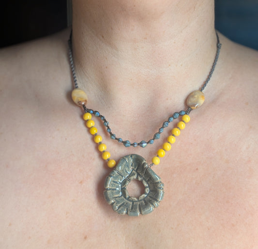 Necklace with a large circular pendant and yellow beads on a person's neck.