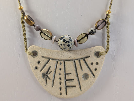 Necklace with a large ceramic pendant and beaded chain on a light gray background