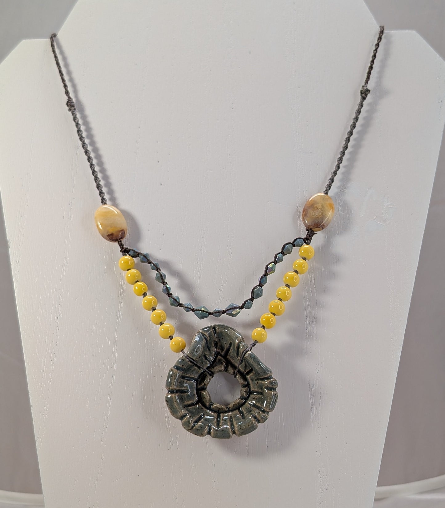 Necklace with a large circular pendant and smaller beads on a white stand