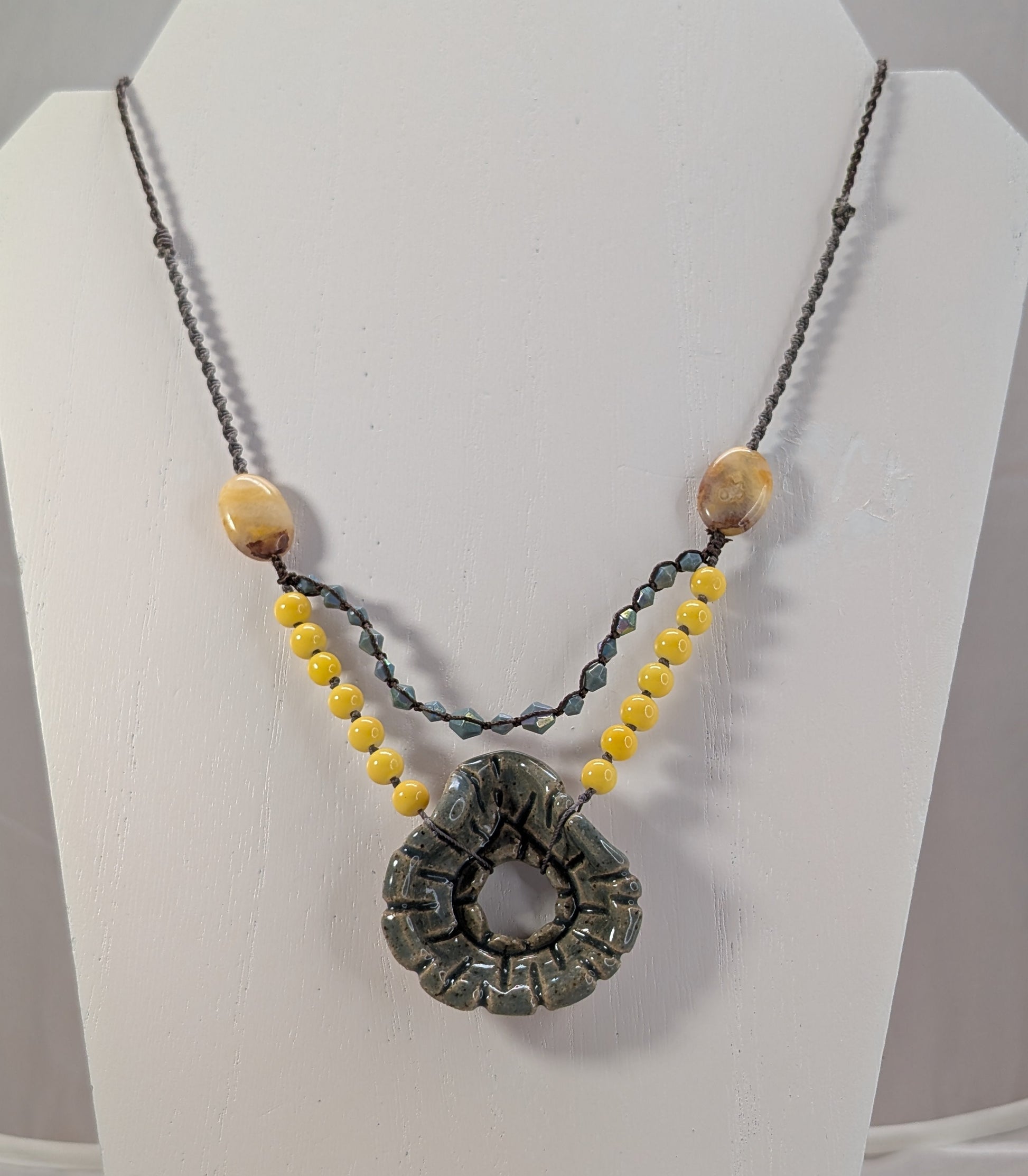 Necklace with a large circular pendant and smaller beads on a white stand