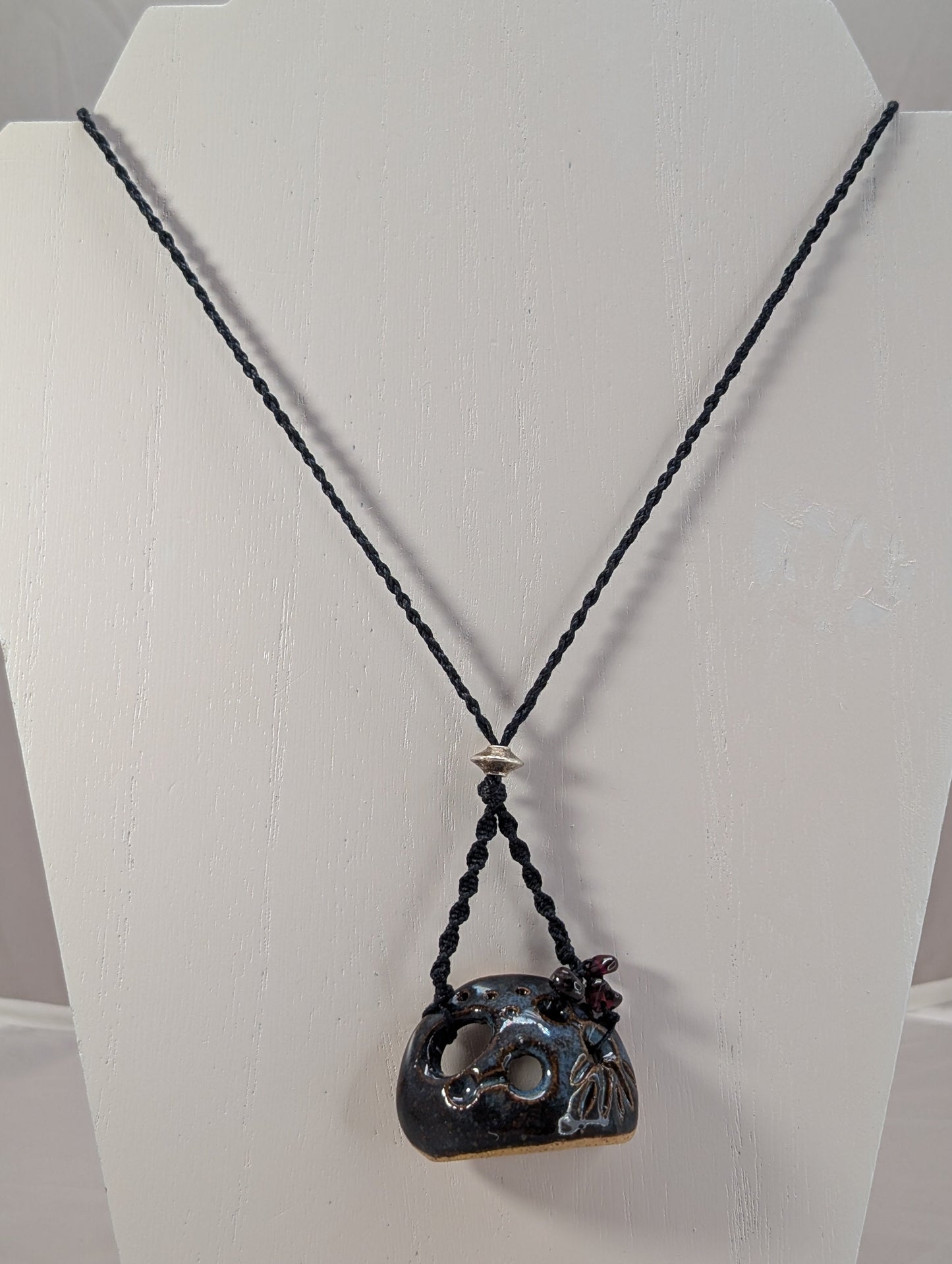 Necklace with a black cord and unique pendant on a white stand.