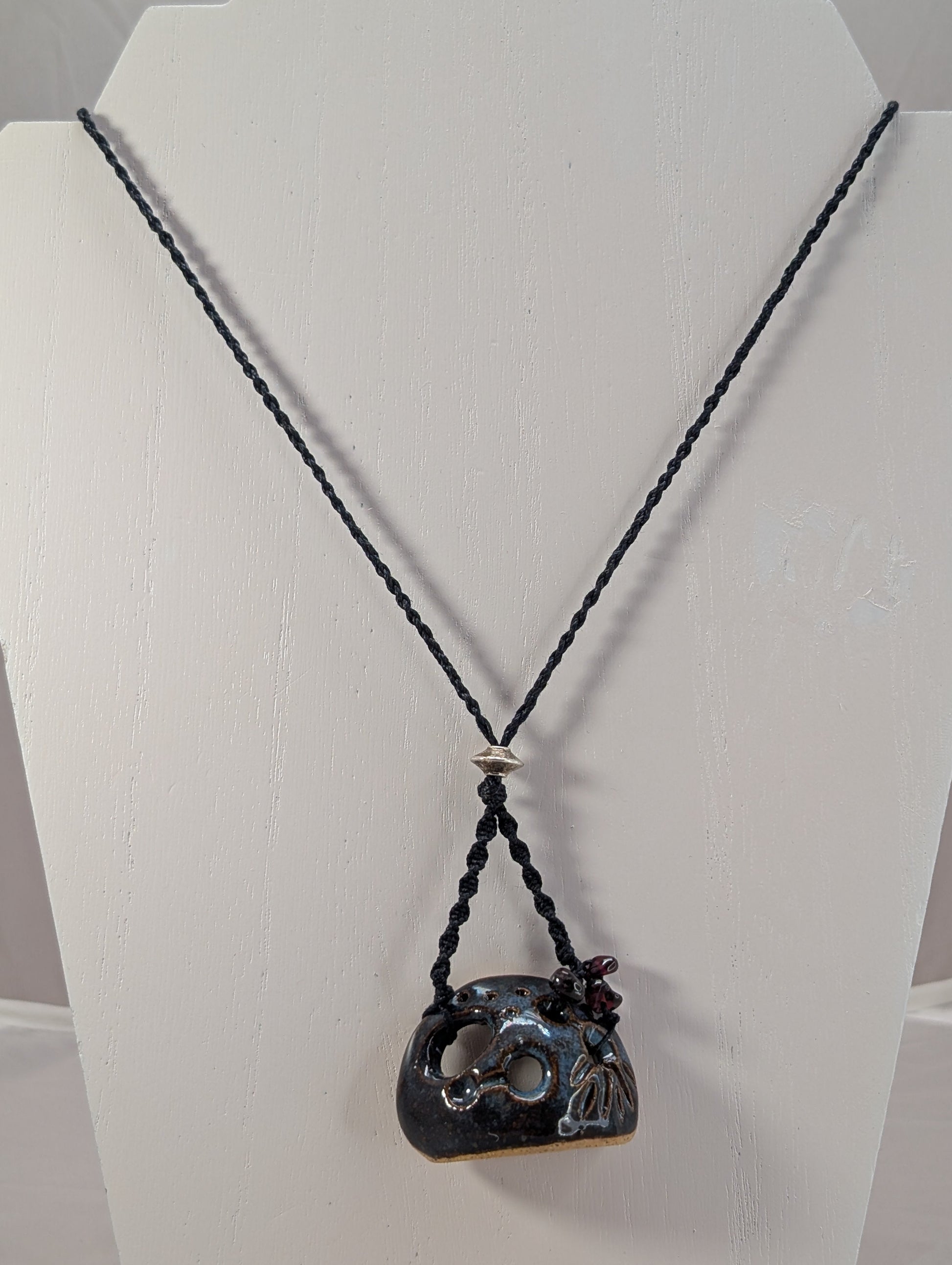 Necklace with a black cord and unique pendant on a white stand.