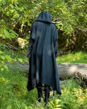 a person wearing a long grey hooded coat walking into the woods