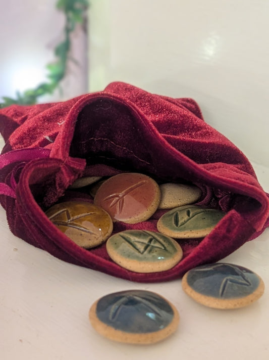 Set of hand-carved ceramic runes on a red drawstring bag 