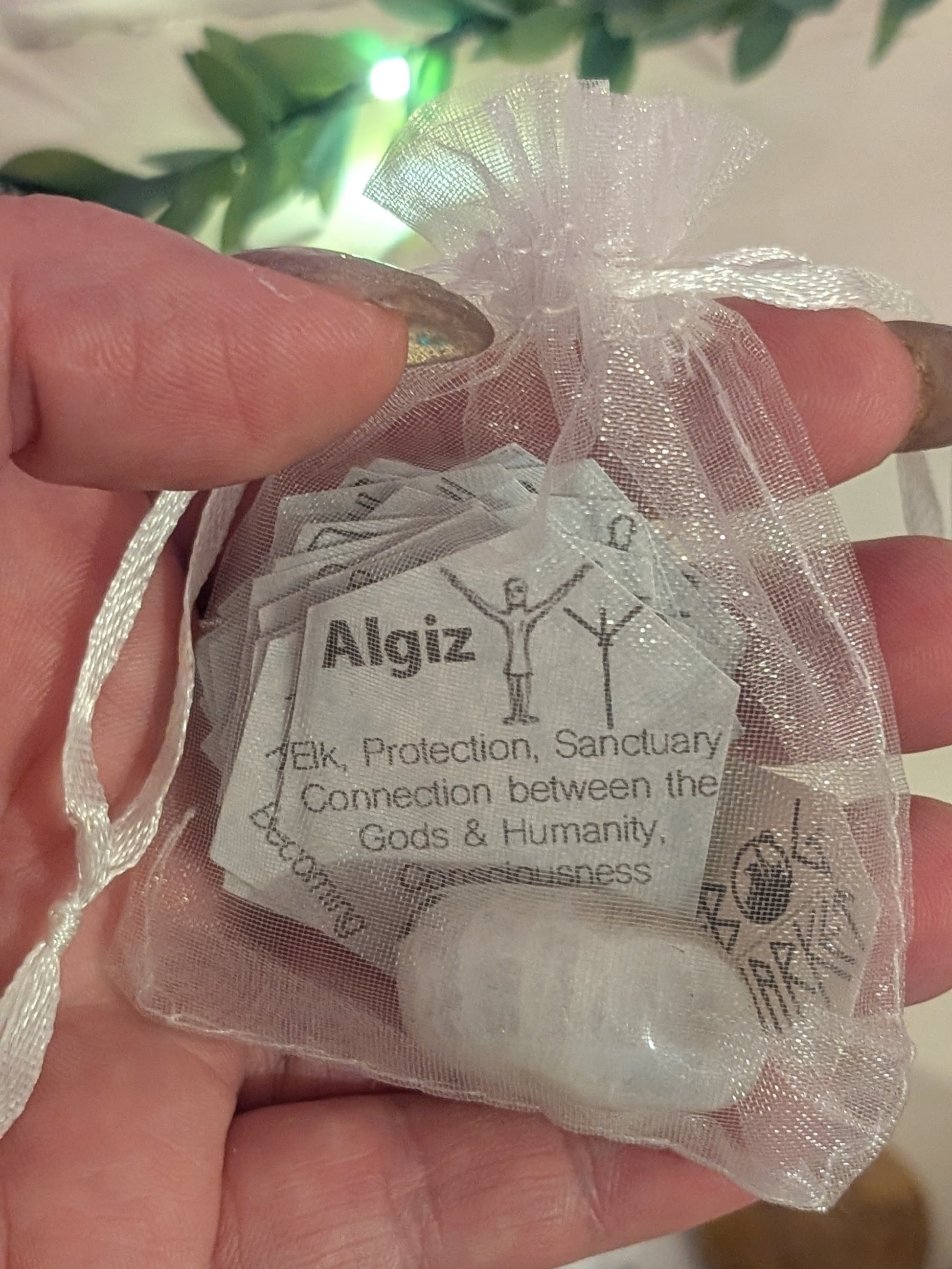 Hand holding a small bag with Algiz rune definition and a charging crystal 