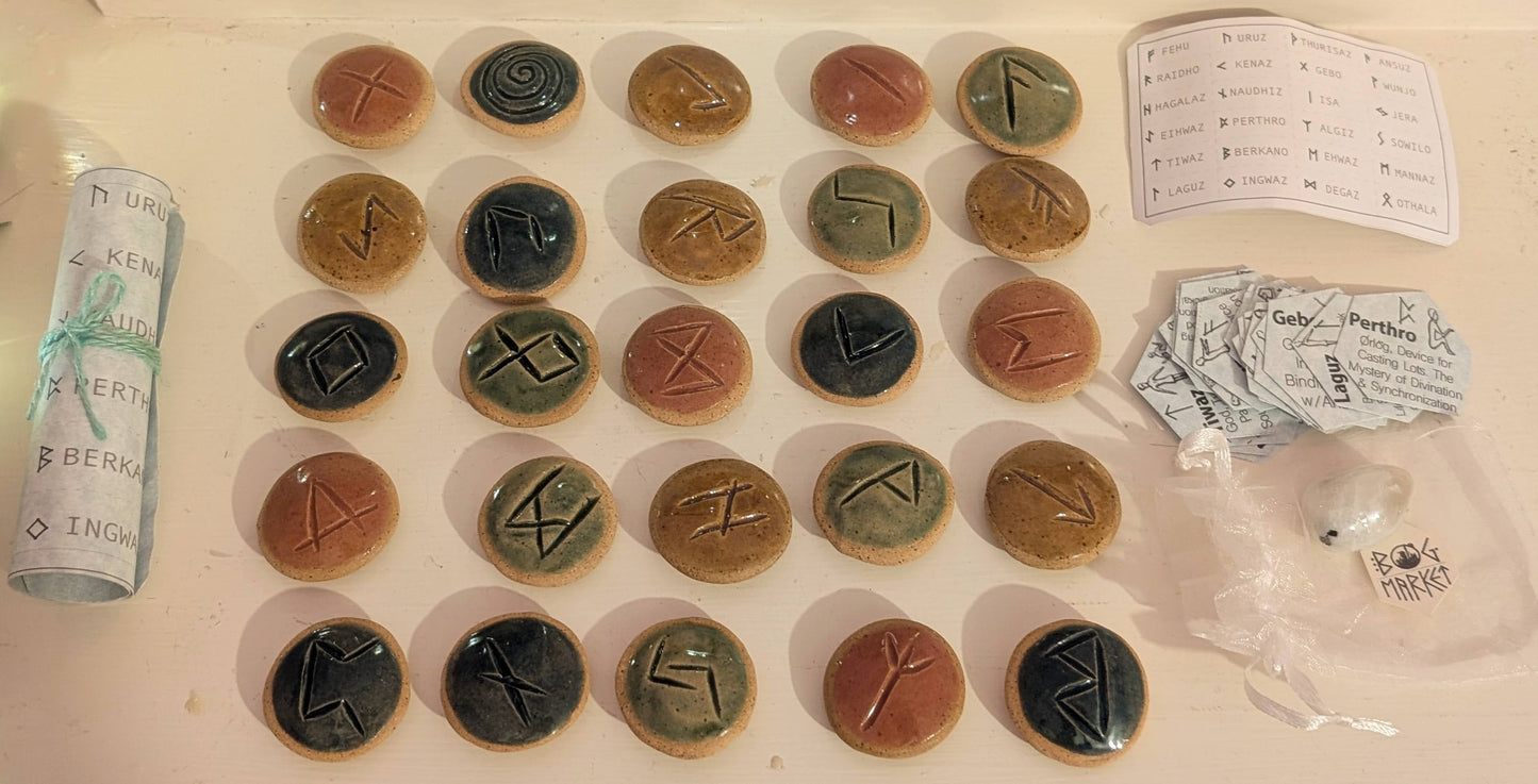 Set of elder futhark ceramic runes on a white surface, accompanied by rune glossary cards and other kit contents