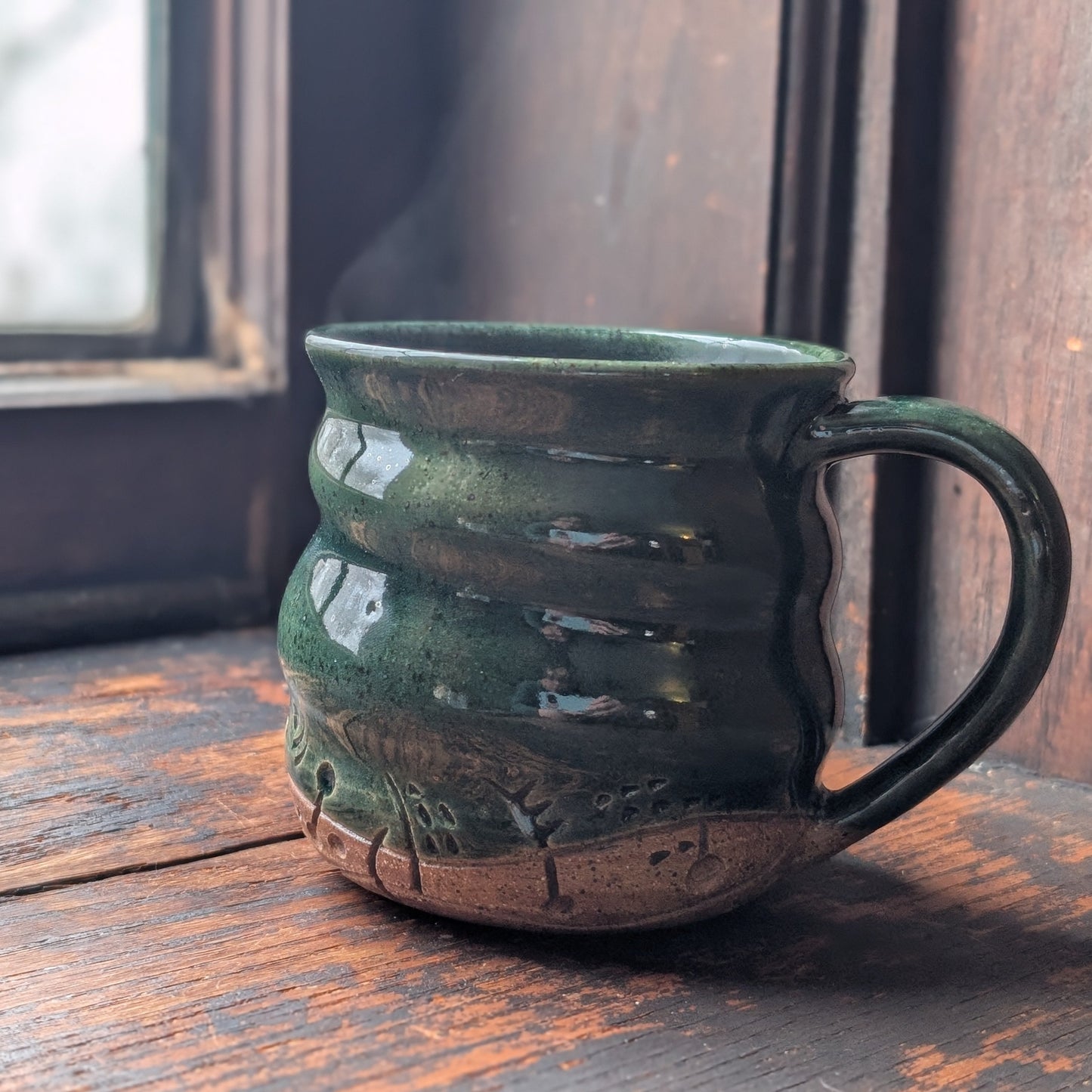 Green ceramic mug on a wooden surface with a blurred window background